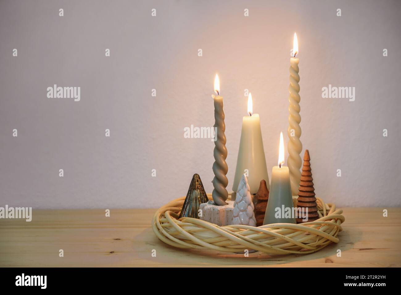 Decorazione semplice dell'avvento in colori naturali con diverse candele e piccoli alberi di Natale artificiali disposti in una corona di falce su un bosco Foto Stock