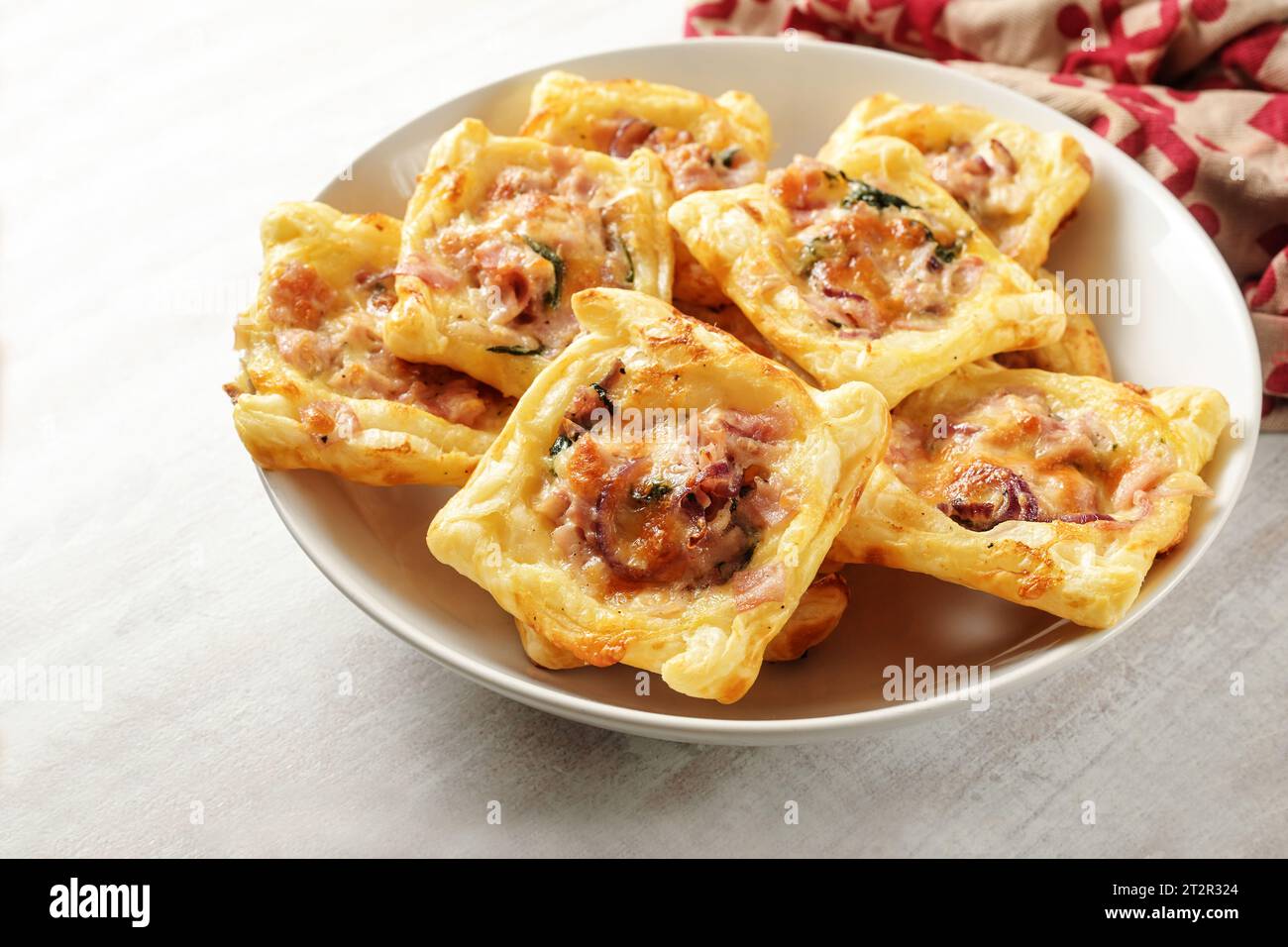 Quadrati di pasta sfoglia al forno con prosciutto, spinaci e formaggio in una ciotola bianca, stuzzichini per un buffet caldo o freddo, spazio per copiare, focalizzazione selezionata, Foto Stock