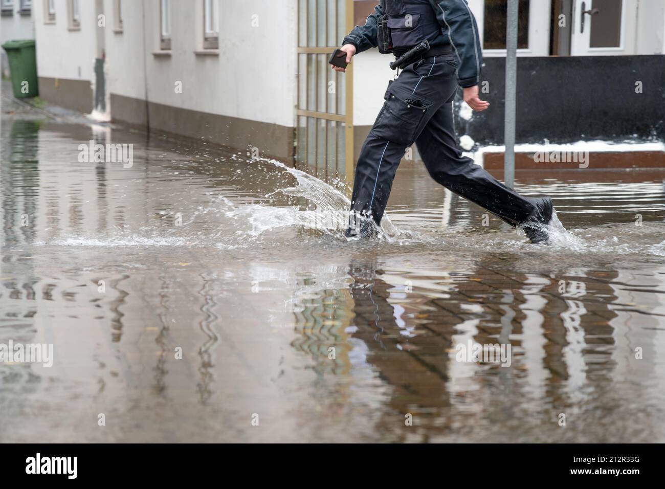 Poliziotto che corre attraverso l'acqua di una strada allagata durante l'alta acqua del fiume Trave nel centro storico di Lubeck, nel Mar Baltico in Germania, c Foto Stock