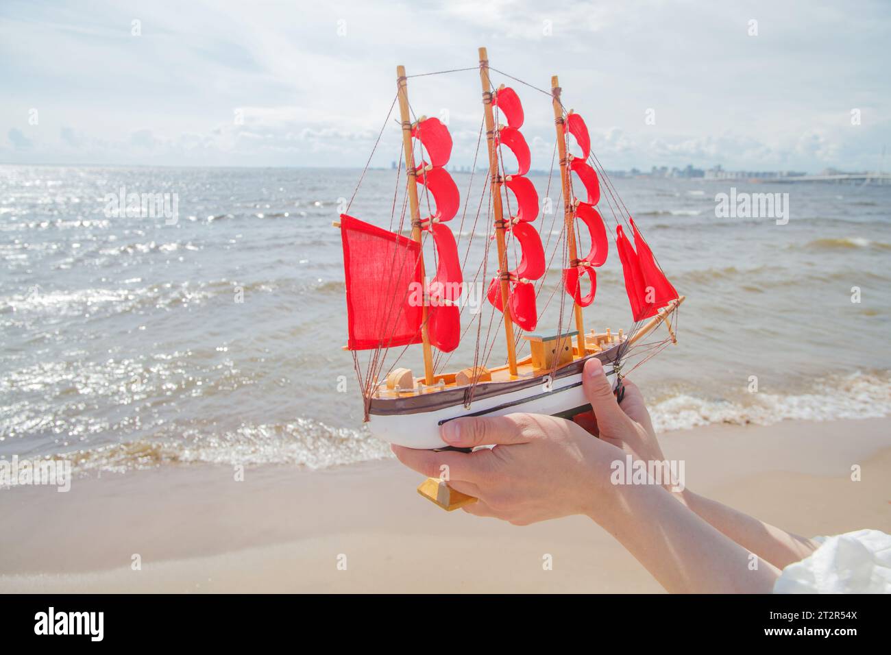 Concetto di viaggio e crociera. Naviga con vele rosse contro il mare, la spiaggia e le nuvole del cielo Foto Stock