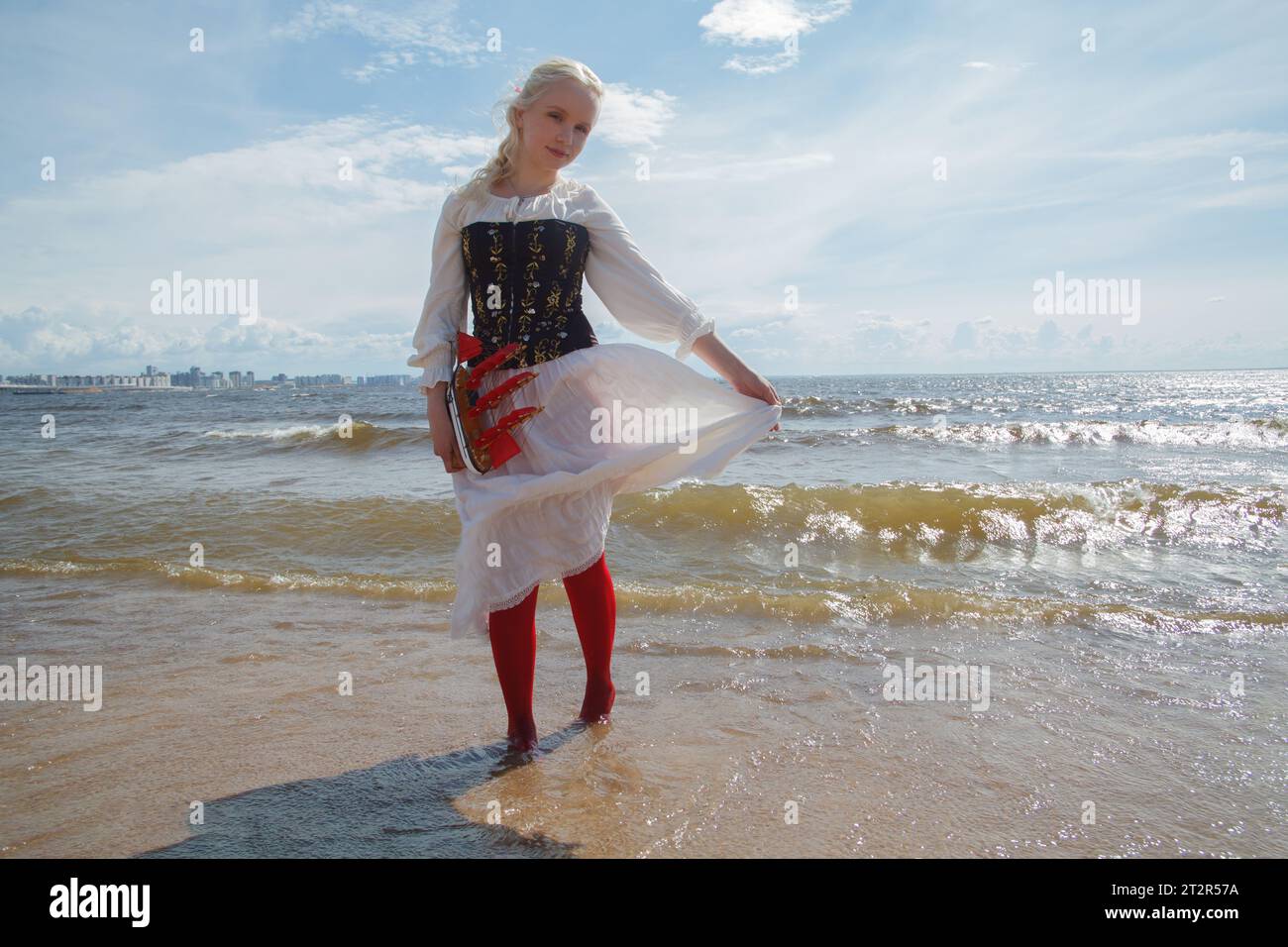 Bella donna in abito vintage che regge una barca a vela rossa contro il mare e il cielo Foto Stock