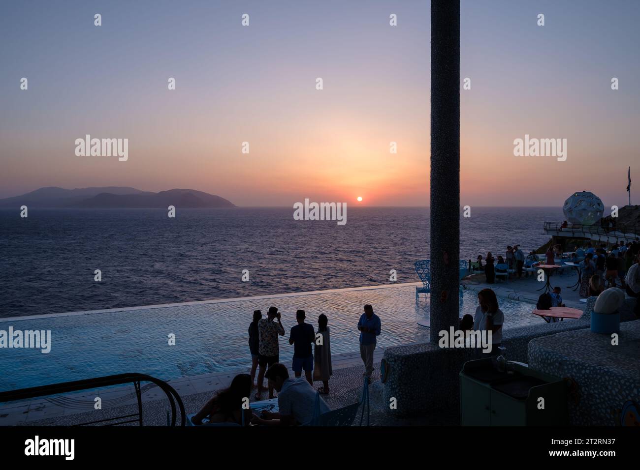 IOS, Grecia - 11 settembre 2023: I giovani si riuniscono intorno alla piscina in un Lounge bar per guardare il tramonto a iOS cicladi Grecia Foto Stock