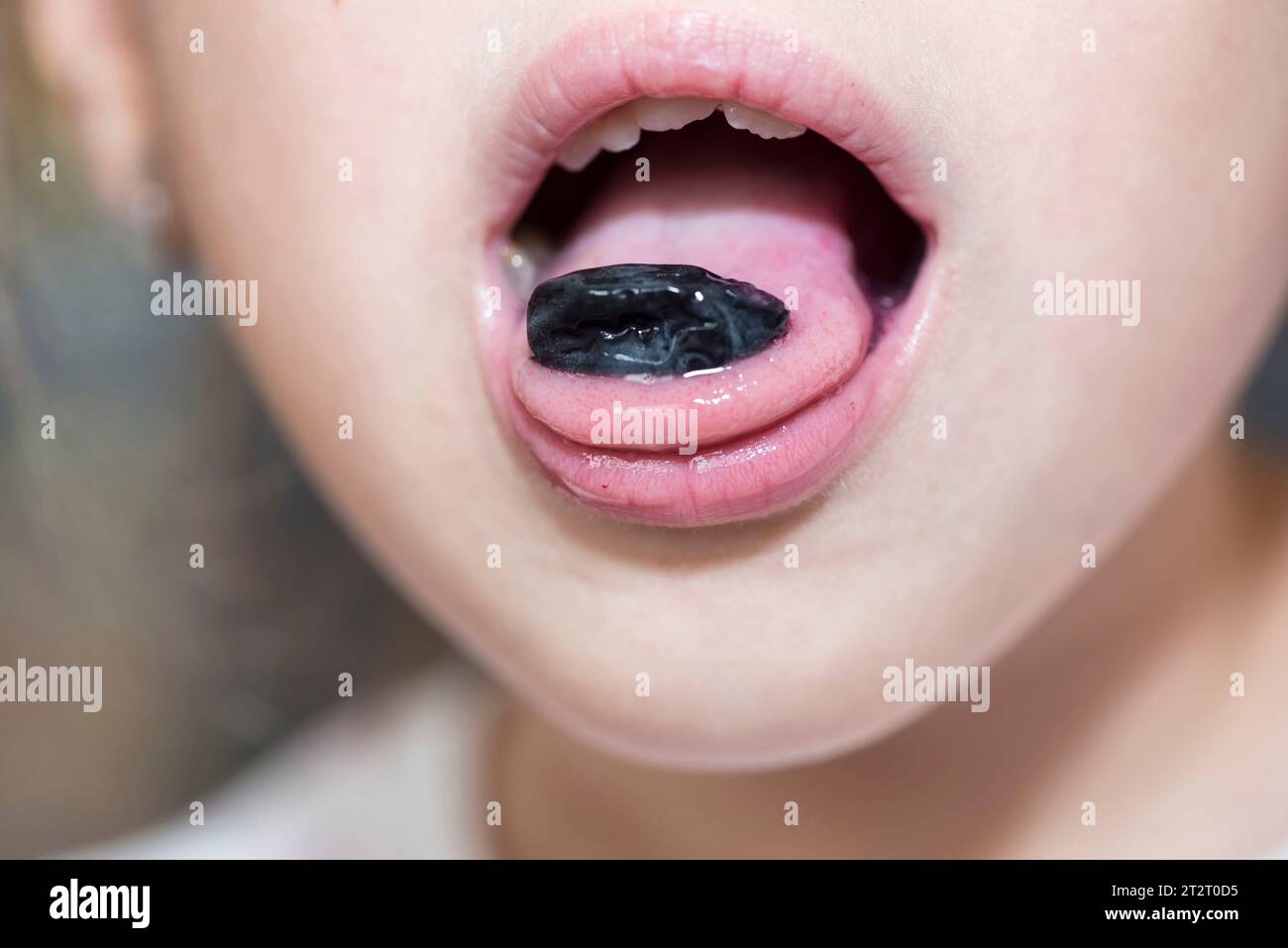 Primo piano della bocca di un bambino con una pelle di uva Foto Stock