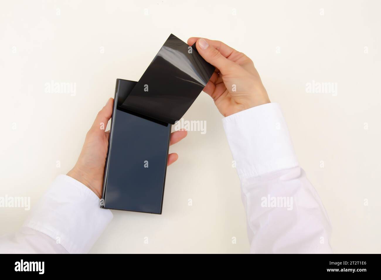 Disimballare il nuovo smartphone. Rimozione della pellicola protettiva nera da un nuovo telefono. Primo piano delle mani di una donna. Sfondo bianco. Smartphone samsung Galaxy S23 Foto Stock