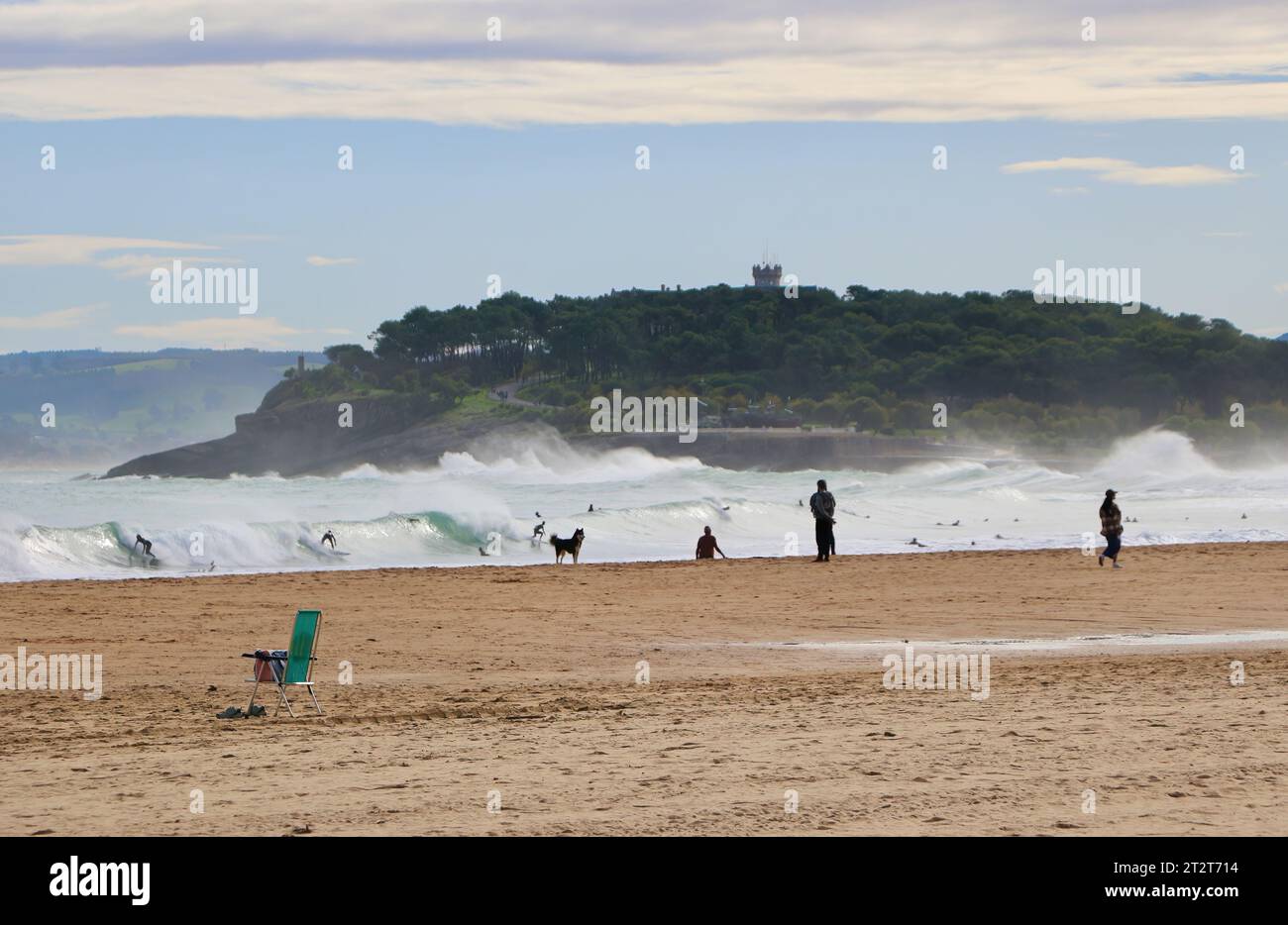 Scarpe sotto una sedia verde sulla spiaggia, surfisti, campeggiatori di cani e il Palazzo della Maddalena in una tempesta mattutina di ottobre Sardinero Santander Cantabria Spagna Foto Stock