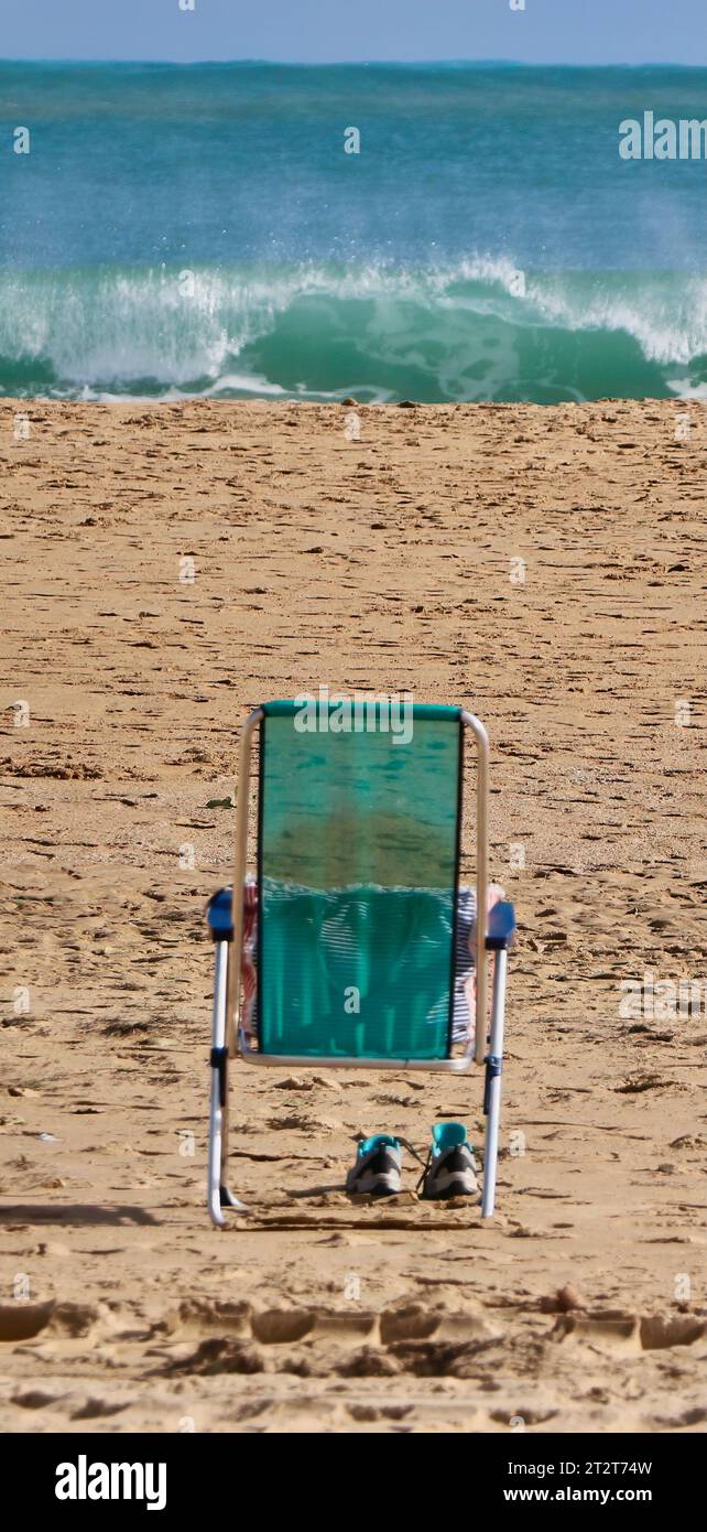 Scarpe sotto una sedia verde sulla spiaggia che guardano verso le onde e l'orizzonte del mare con nessuno Sardinero Santander Spagna Foto Stock