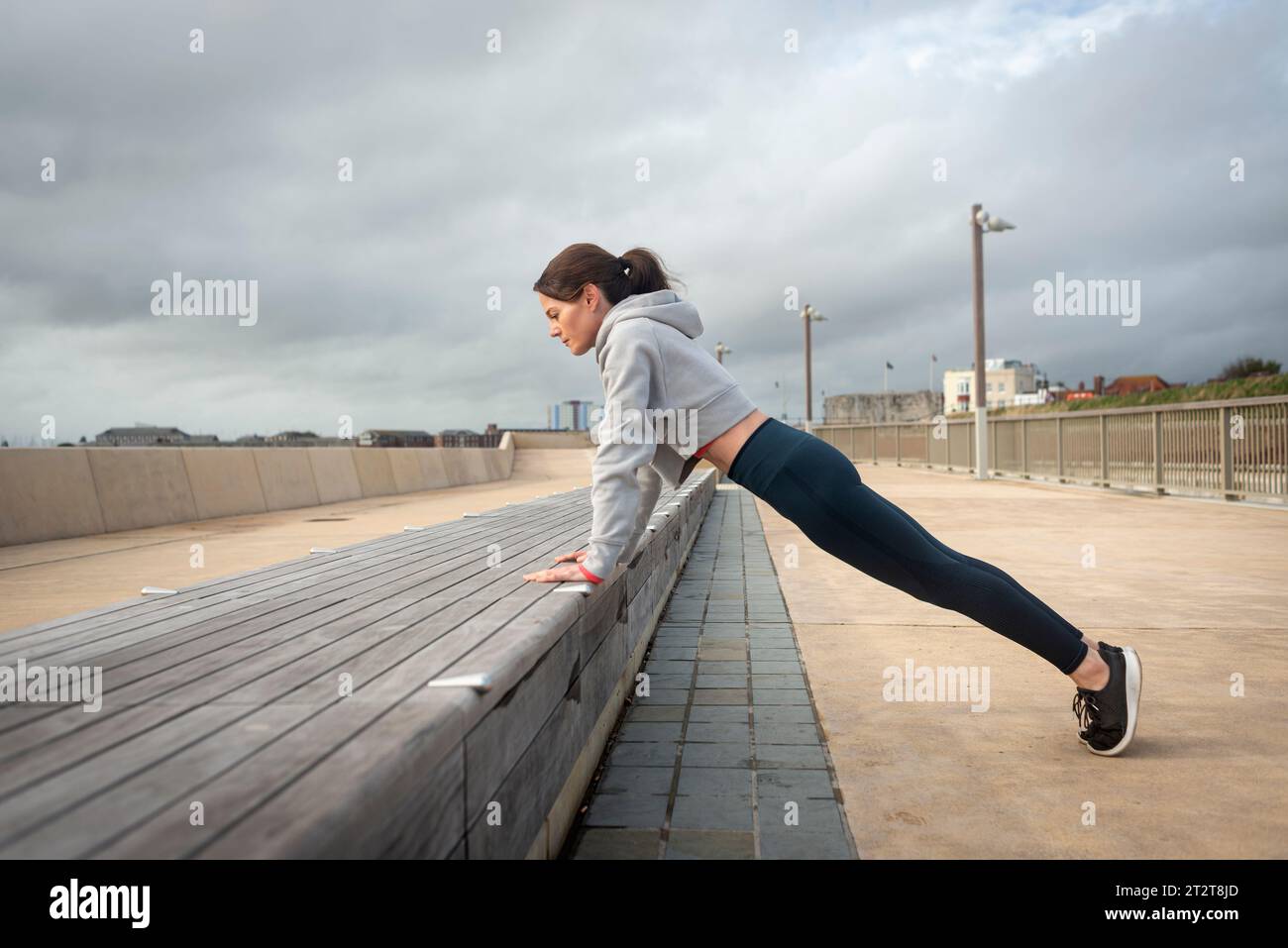 Donna sportiva che fa pressione su una panca di legno. Allenamento all'aperto Foto Stock