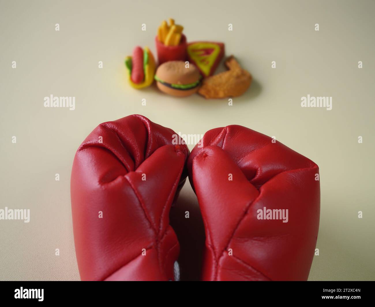 Immagine ravvicinata di guanto da boxe e cibi spazzatura come hamburger e patatine fritte. Combattere le cattive abitudini alimentari. Foto Stock