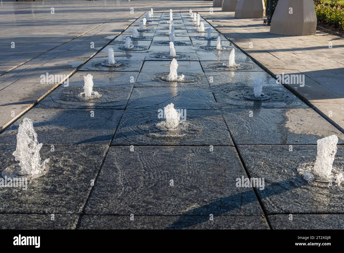 Spruzzi d'acqua nel parco con una piccola fontana situata sul marciapiede Foto Stock