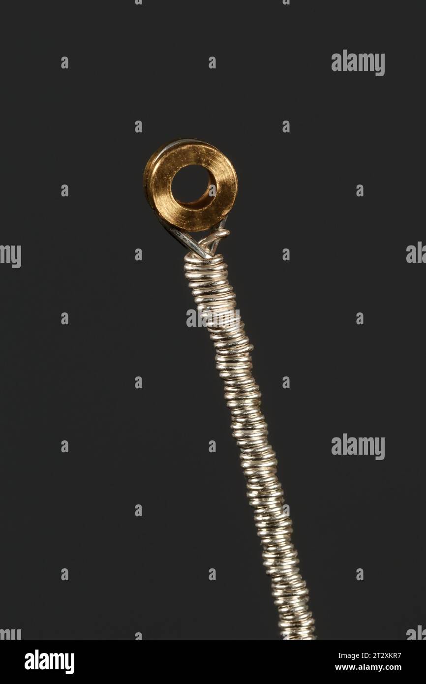 Supporto inferiore di una corda di chitarra argentata su sfondo scuro. Fotografia macro Foto Stock