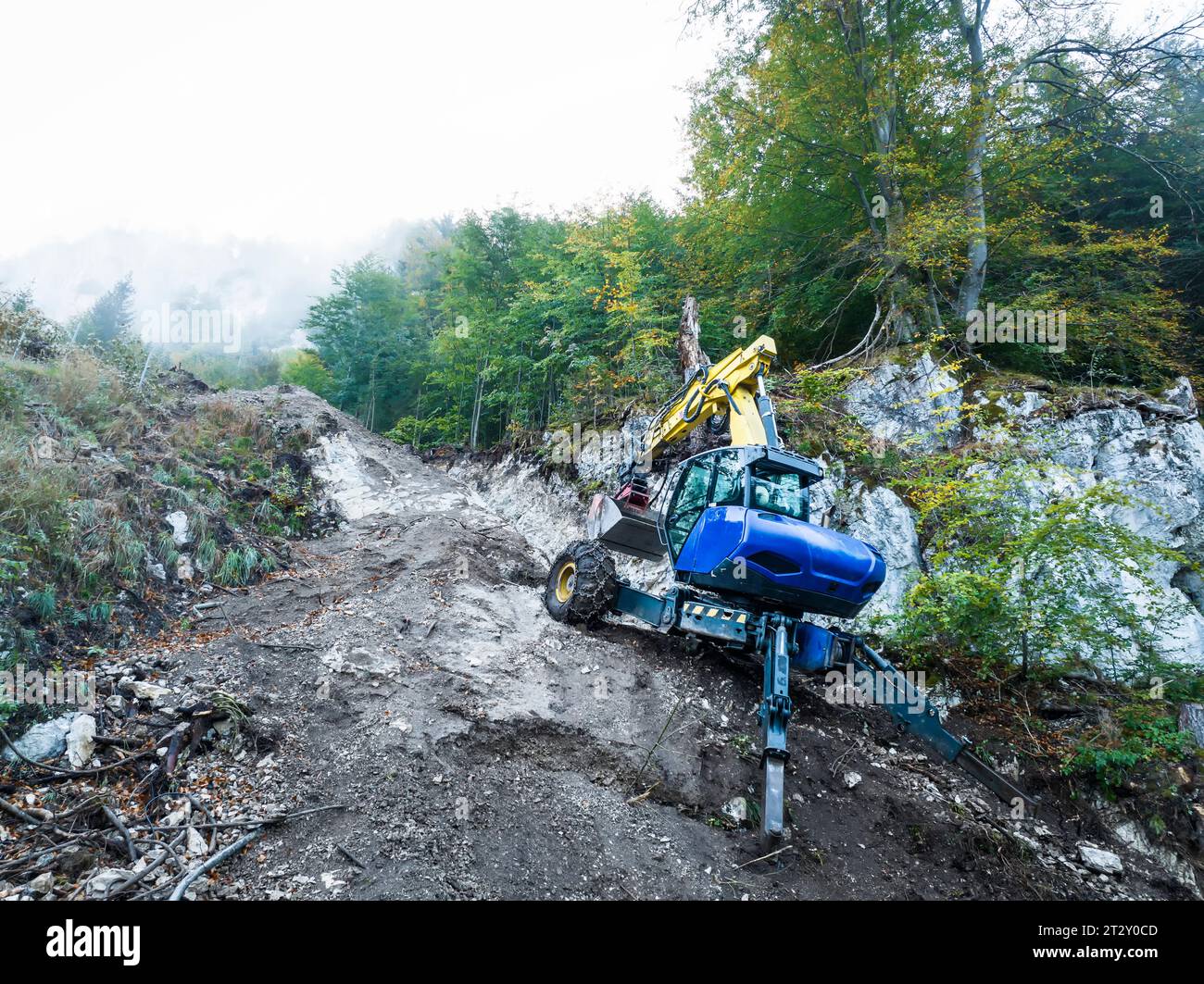 Escavatore a piedi o scavato in un terreno roccioso molto ripido e difficile nella foresta montana mentre scavate una trincea a fune Foto Stock