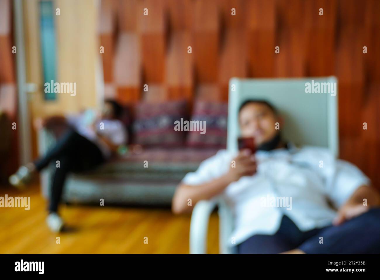 Un'affascinante composizione sfocata che cattura la scena dinamica di due uomini impegnati nell'uso del proprio smartphone seduti su sedie e divano Foto Stock