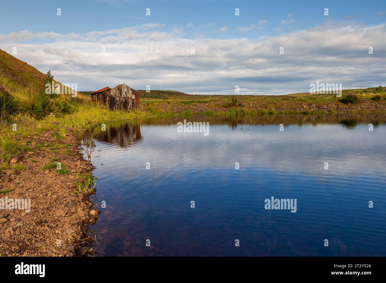 Una rovina di una baracca ai margini di un lago in Scozia in una soleggiata mattinata estiva durante una mattinata estiva Foto Stock