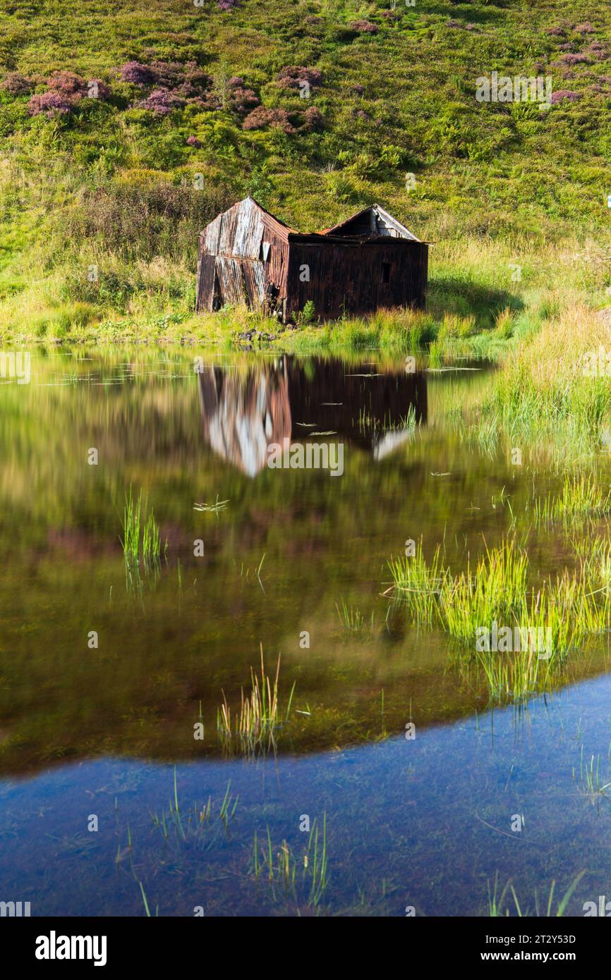 Una rovina di una baracca ai margini di un lago in Scozia in una soleggiata mattinata estiva durante una mattinata estiva Foto Stock