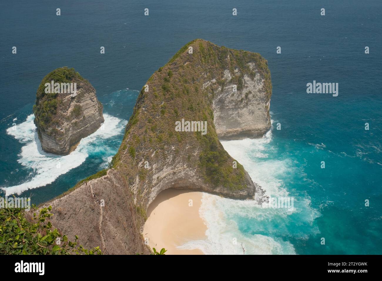 Scopri l'ampia bellezza di Kelingking Beach in questa vista panoramica, dove le acque schiumose accarezzano dolcemente la costa sabbiosa. Foto Stock