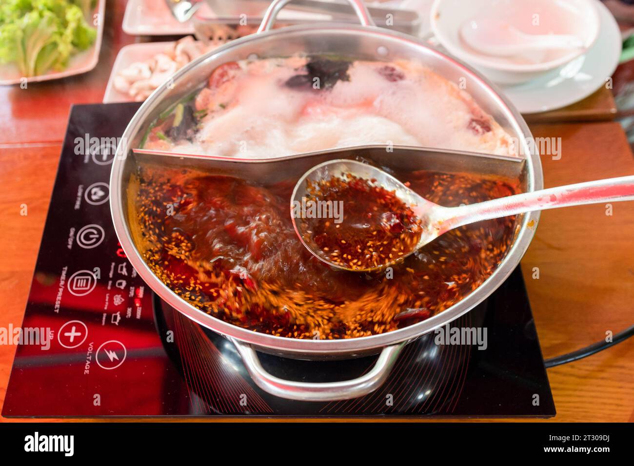 cucina cinese - cucchiaio con brodo speziato sopra il wok durante la cottura della zuppa di pentole calde Foto Stock