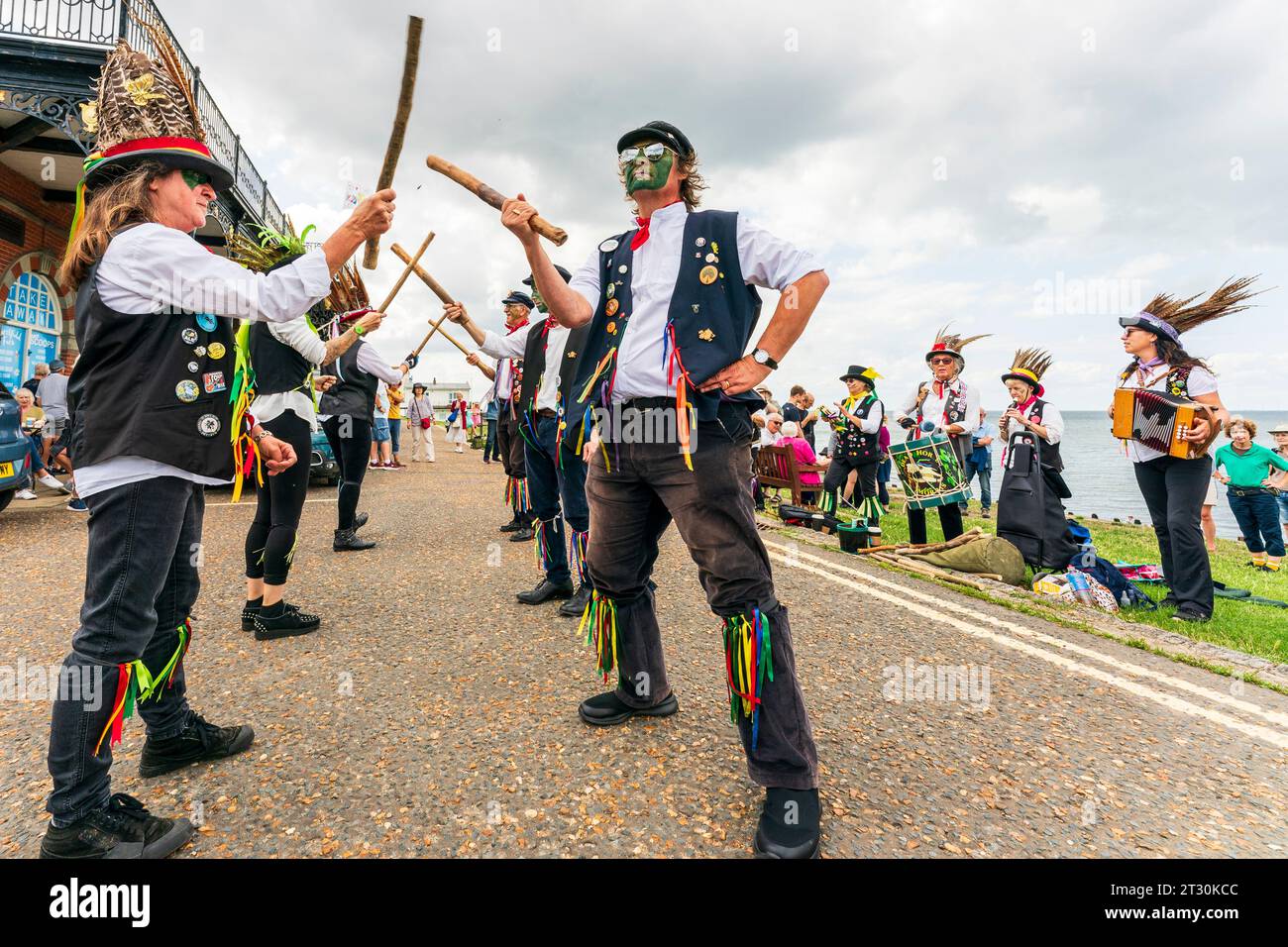 Dead Horse Morrismen che tiene dei bastoncini, in due linee, ballando sul lungomare con la band dietro di loro, nella località turistica del Kent, Herne Bay. Cielo grigio. Foto Stock