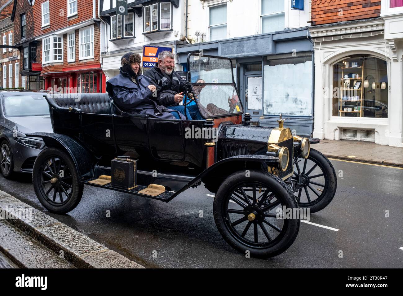 Una coppia di anziani che guidano Un'auto d'epoca durante alcune condizioni meteorologiche avverse, High Street, Lewes, East Sussex, Regno Unito. Foto Stock
