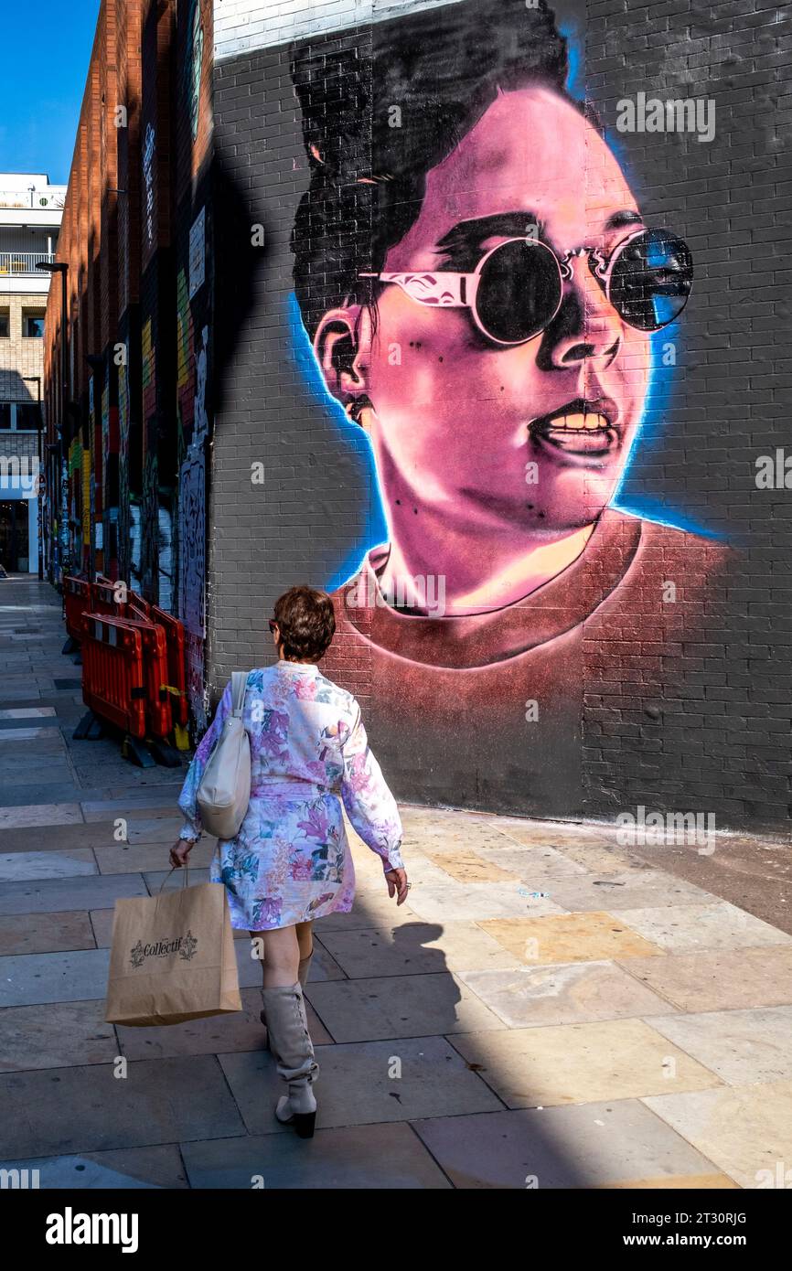 Una donna cammina davanti a un po' di colourful Street Art, Shoreditch, Londra, Regno Unito. Foto Stock