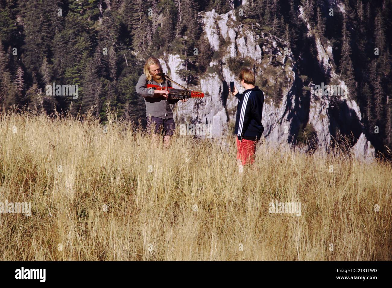 bionda giocatore di nyckelharpa che si esibisce nel paesaggio del Parco Nazionale di Sutjeska e una persona che registra video con il cellulare, Bosnia An Foto Stock
