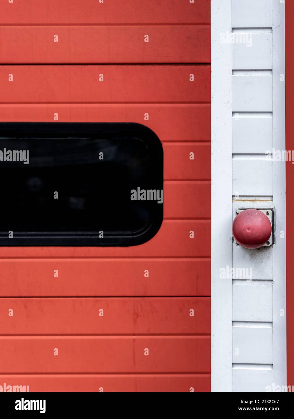 Parte di una porta rossa e bianca della stazione dei vigili del fuoco, primo piano del pulsante di apertura e finestra colorata Foto Stock