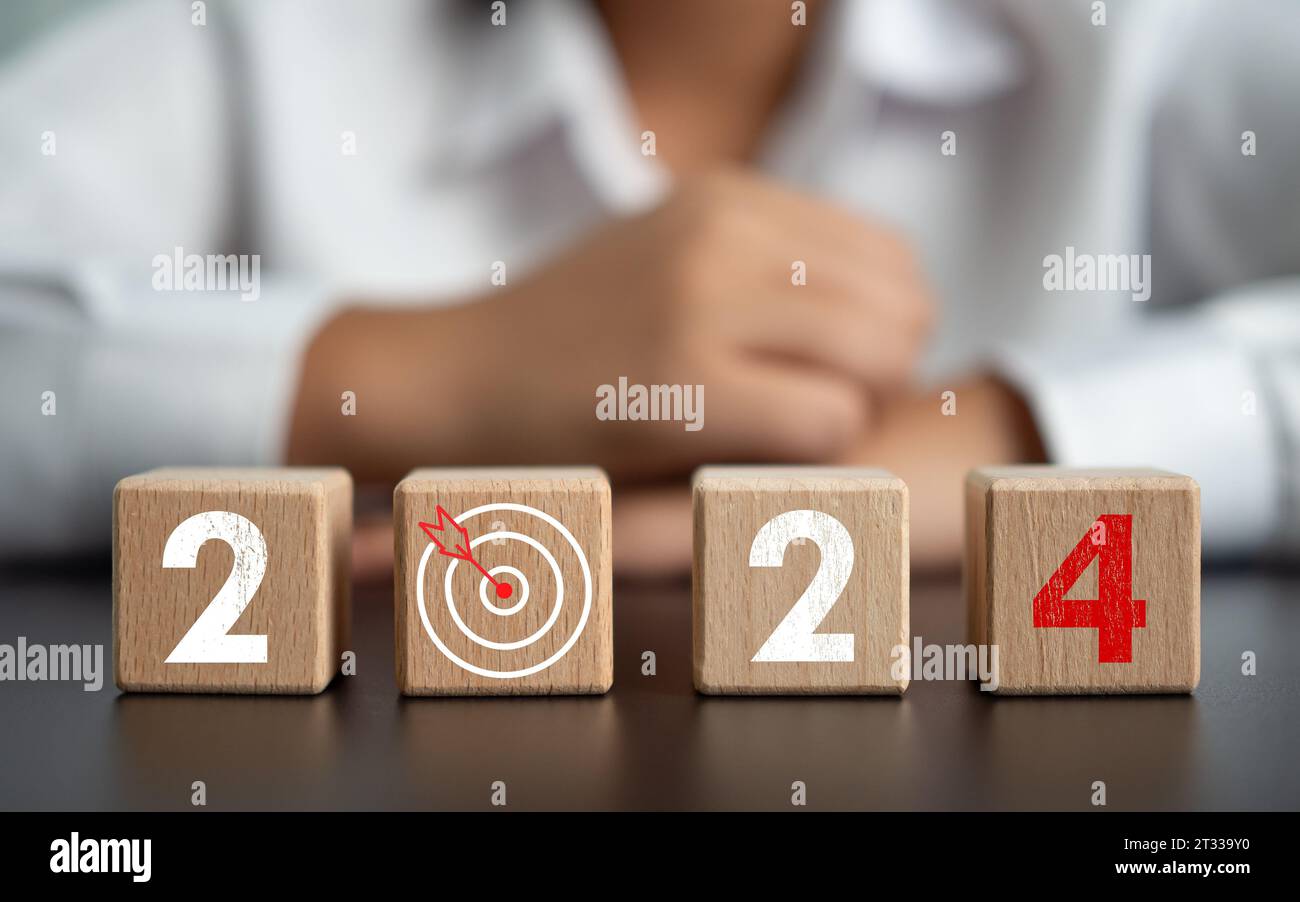 Blocchi di legno fiancheggiati da lettere dell'anno 2024 con una freccetta e un uomo d'affari sullo sfondo è considerato fissare obiettivi per il 2024 ed è Foto Stock