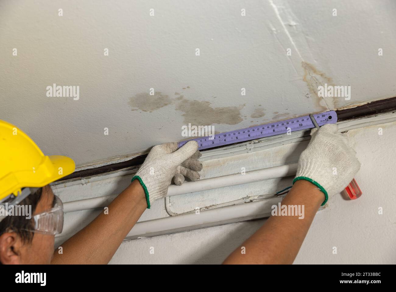Il lavoratore ripara il tubo che perde nel soffitto, primo piano di una macchia sul soffitto. Foto Stock