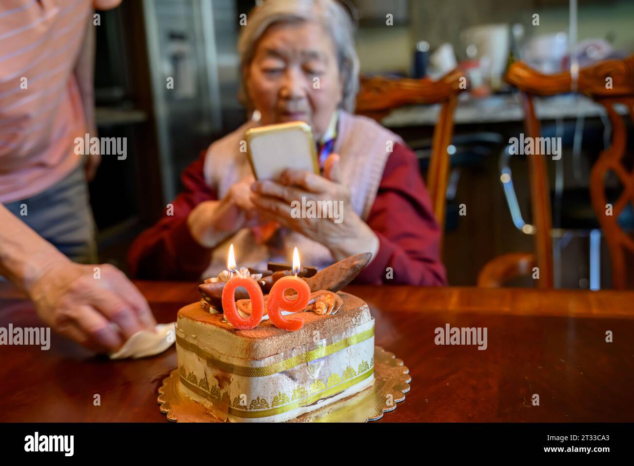 Donna anziana che scatta foto da smartphone di una torta che festeggia il suo 90° compleanno. Foto Stock
