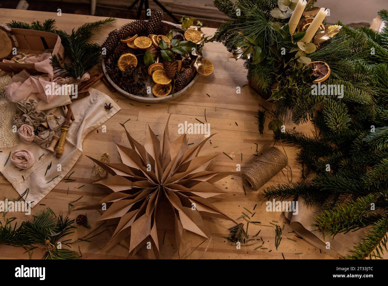 Su un tavolo di legno si trova una stella fatta a mano in carta artigianale fai da te. Decorazioni naturali per la casa per Natale. Intorno alla stella ci sono candele, rami di abete, strumenti, Foto Stock