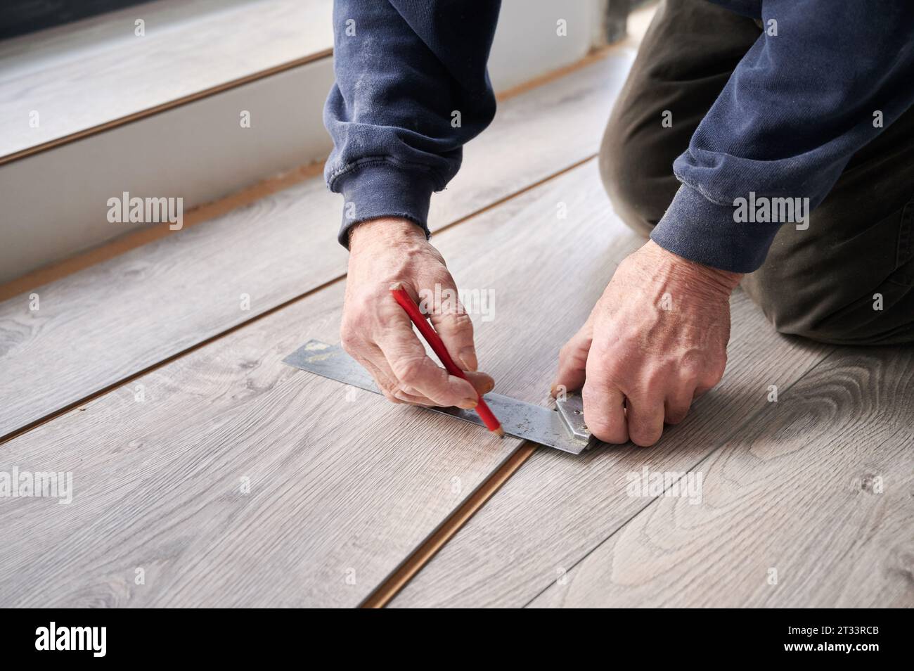 Primo piano delle mani dell'uomo utilizzando un righello metallico e una matita mentre disegna la linea sulla tavola laminata. Lavoratore edile maschio che misura il pannello di legno laminato per l'installazione a pavimento. Concetto di ristrutturazione della casa. Foto Stock