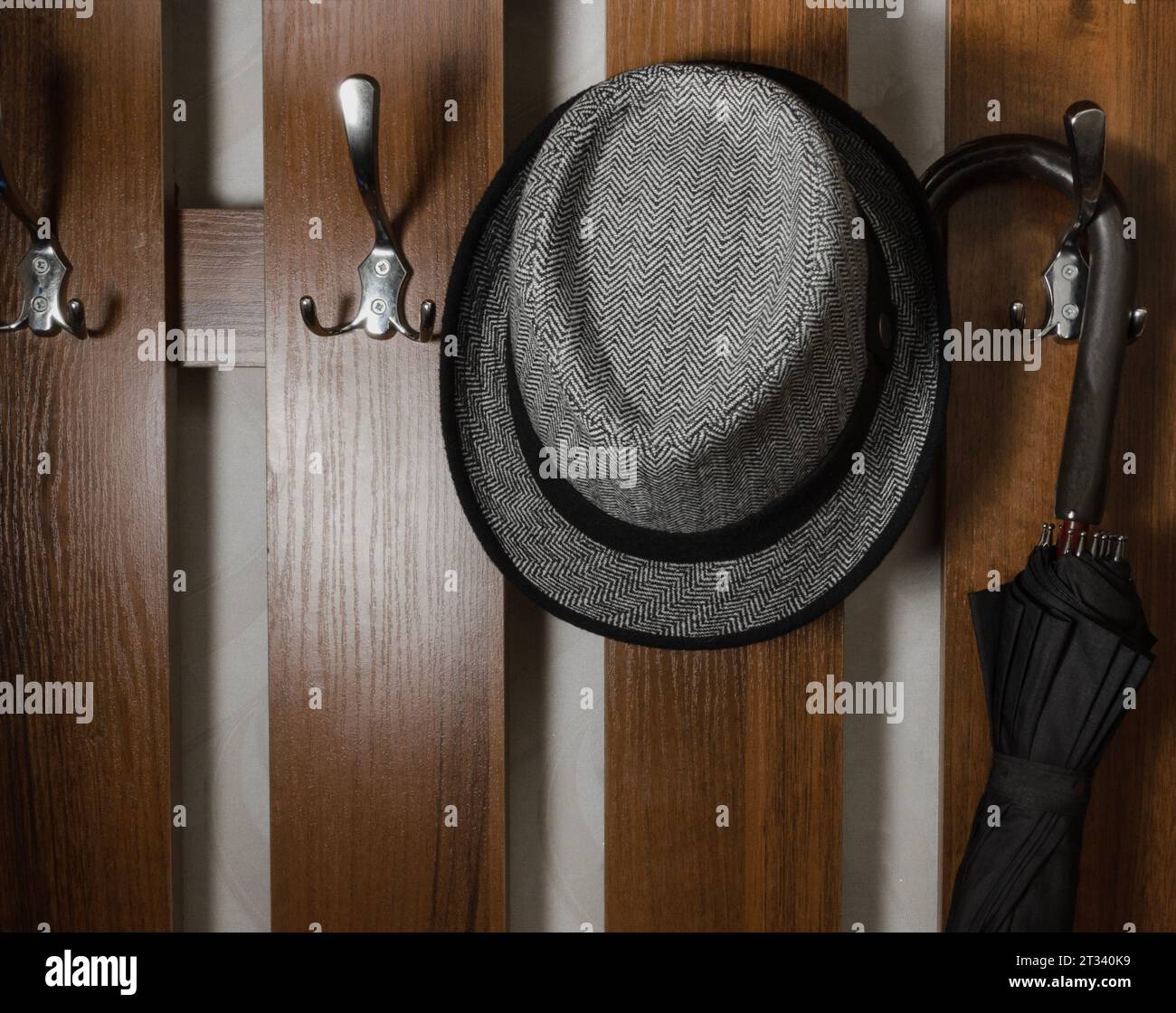 Ombrello nero e cappello leggero su un gancio di legno marrone alla parete Foto Stock