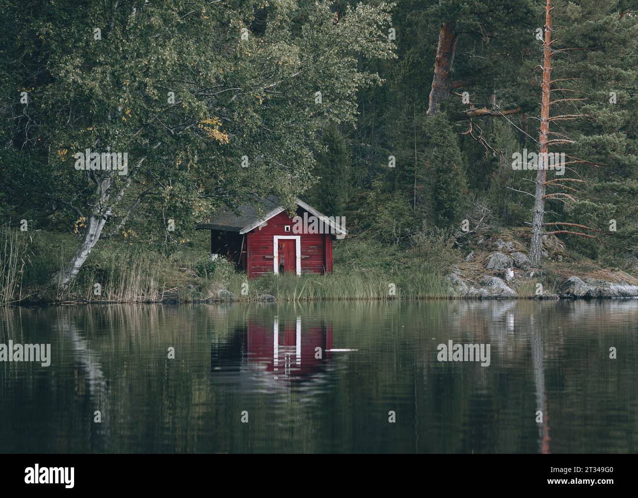 Piccola casa di legno rossa sulla riva di un lago in Finlandia Foto Stock