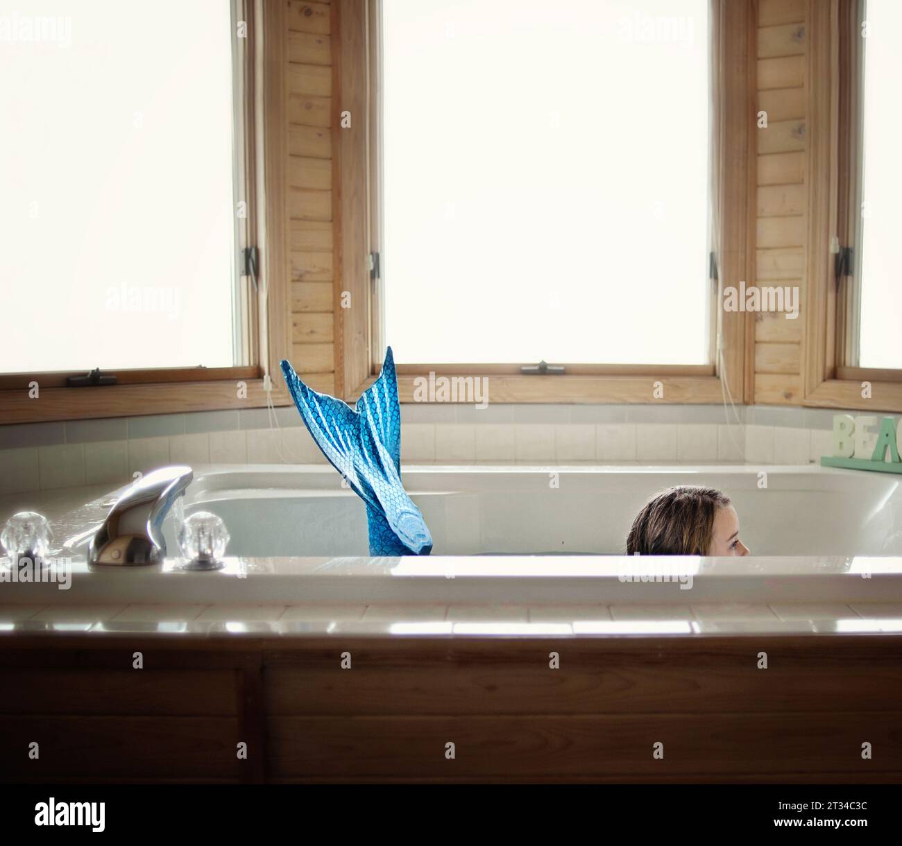 Bambina che indossa la coda di sirena blu nella vasca idromassaggio Foto Stock