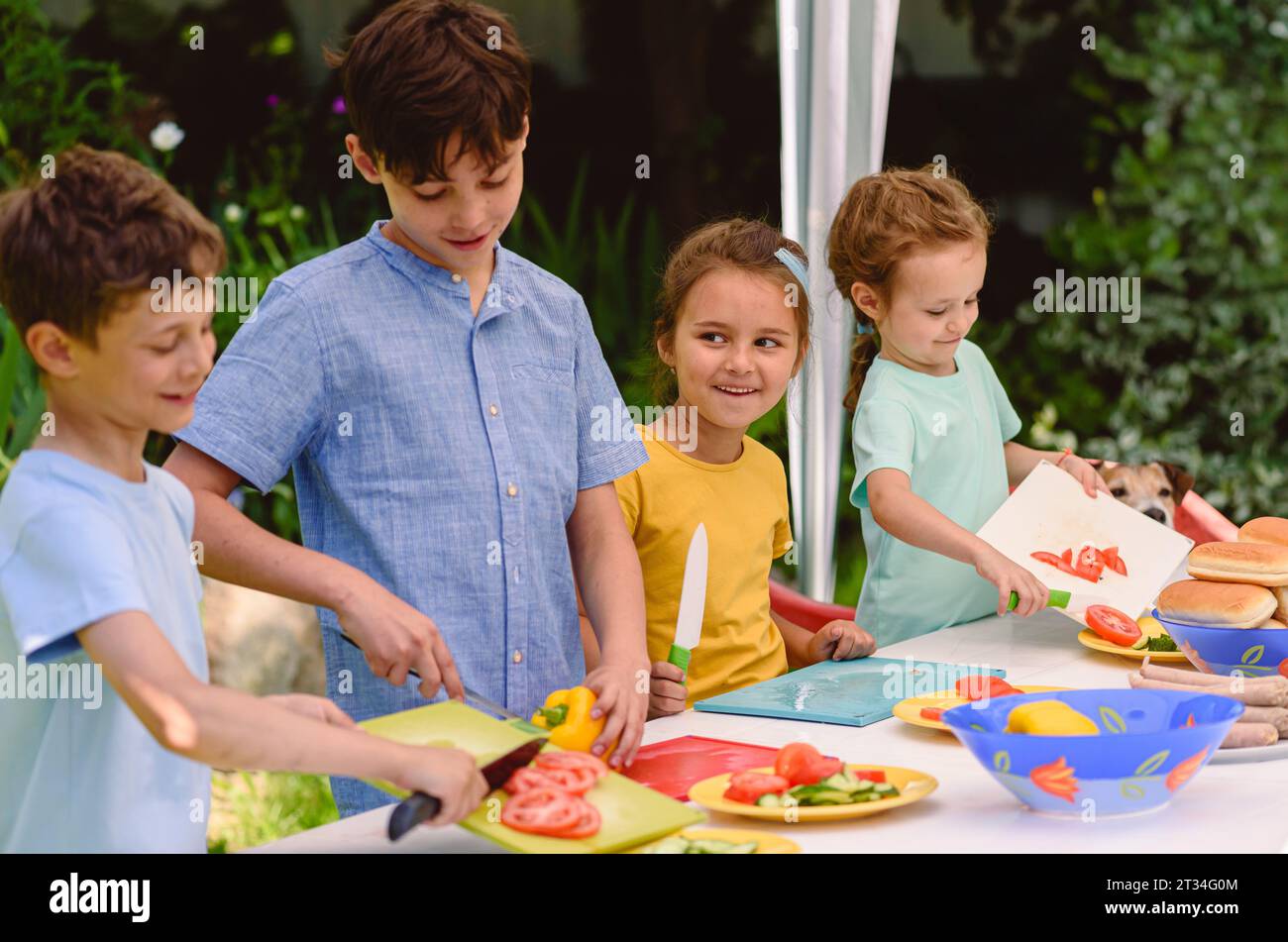 Bambini felici che cucinano insieme hot dog e verdure per le feste all'aperto Foto Stock