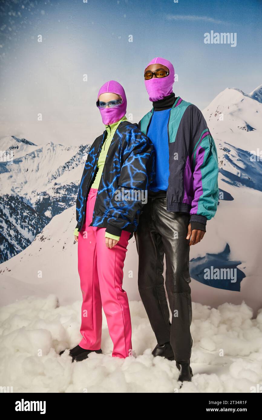 coppia multiculturale alla moda in abiti caldi con balaclavi rosa e occhiali da sole, concetto invernale Foto Stock
