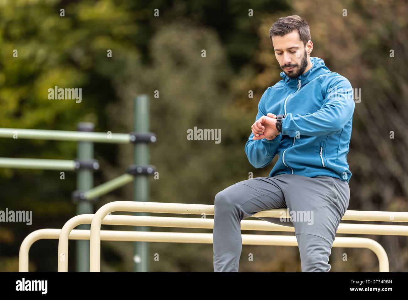 Un giovane atleta siede sui bar della natura e monitora la sua attività su un orologio intelligente. Foto Stock