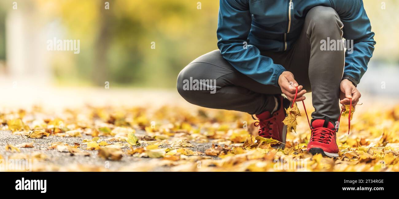 Una vista ravvicinata delle mani di un atleta che si lega i lacci delle scarpe prima di correre in un parco autunnale. Foto Stock