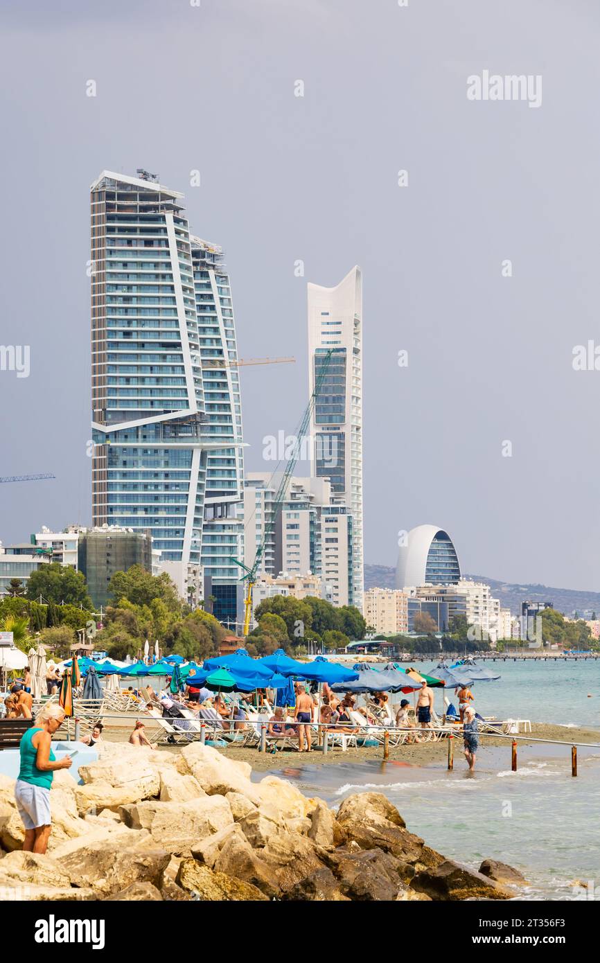 Turisti sulla spiaggia con alti edifici di sviluppo. Uno, Trilogy e The Oval sul lungomare di Limassol, Cipro Foto Stock