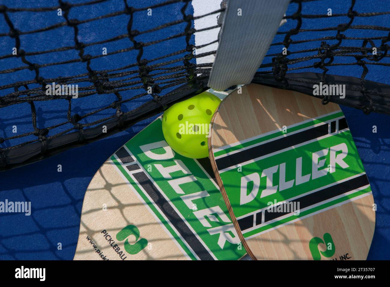 West Islip, New York, USA - 17 luglio 2023: Guardando in basso due racchette di picchettio alla rete da tennis con una palla a frusta da vicino. Foto Stock