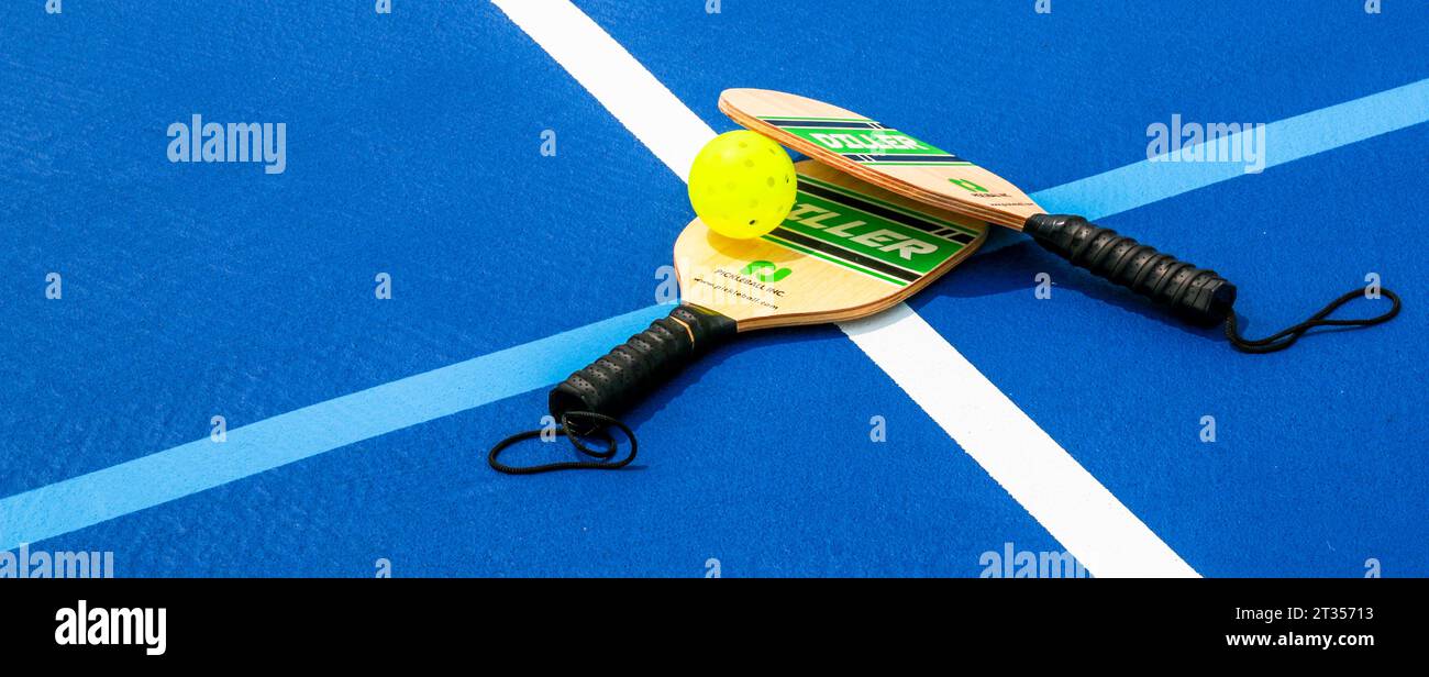 West Islip, New York, USA - 17 luglio 2023: Due pagaie da picchettio con una palla da frusta florecente adagiata su due linee su un campo da tennis da basket blu. Foto Stock