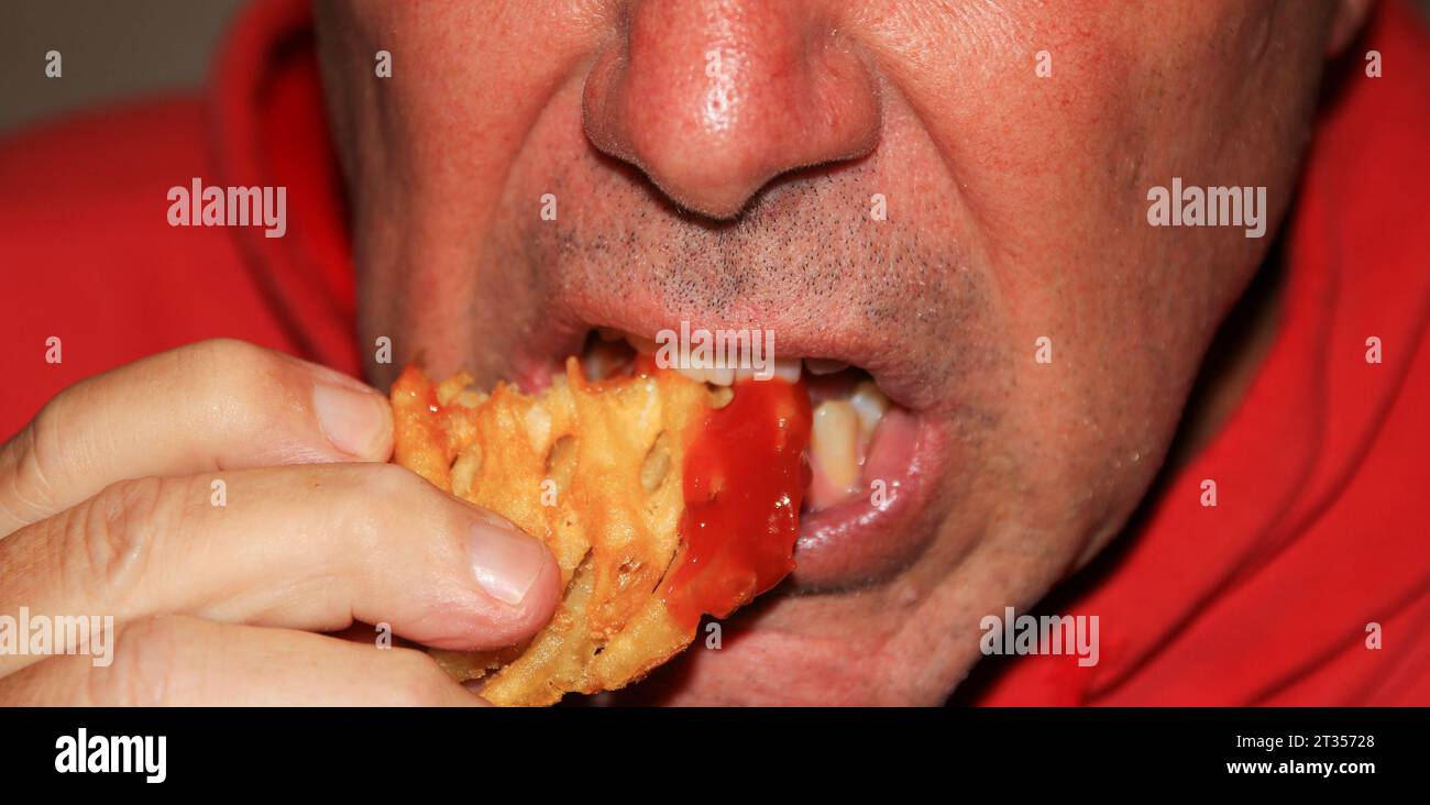Primo piano di un uomo che mangia una patatina fritta con ketchup mettendola in bocca. Foto Stock