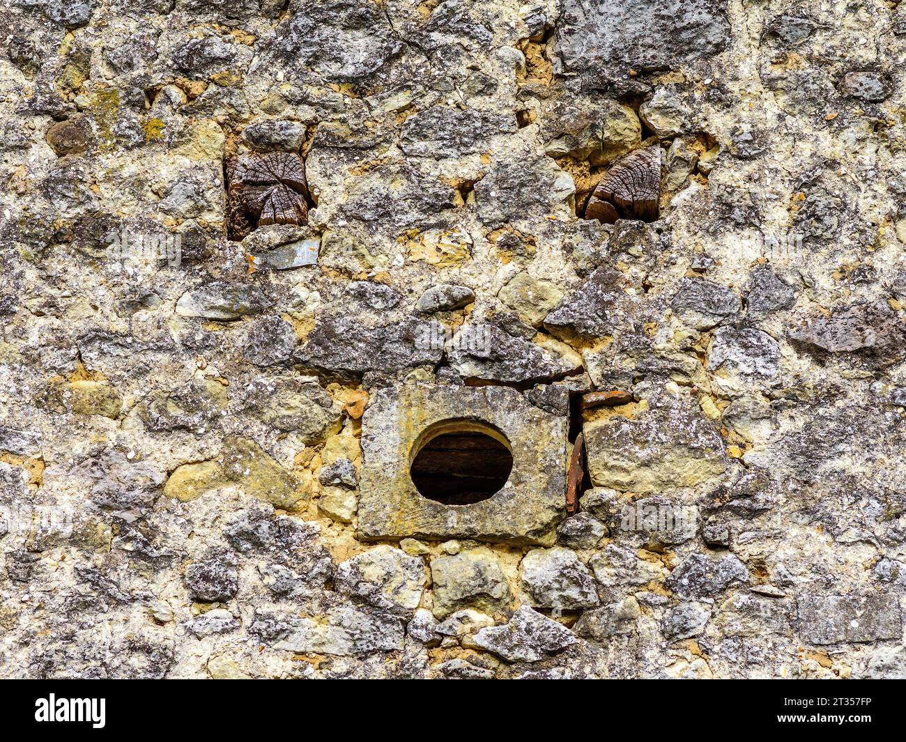Piccolo foro di ventilazione rotondo e estremità di travi in legno che creano un "volto divertente" nel vecchio muro di pietra - Francia centrale. Foto Stock