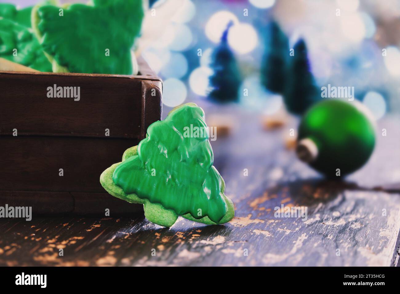 Biscotti glassati a forma di albero di Natale o biscotti con glassa verde su un tavolo rustico. Messa a fuoco selettiva con primo piano e sfondo sfocati. Foto Stock