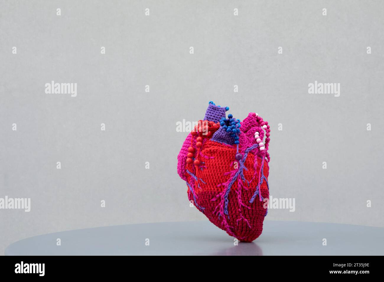 Cuore in lana tenuto sul tavolo su sfondo grigio Foto Stock