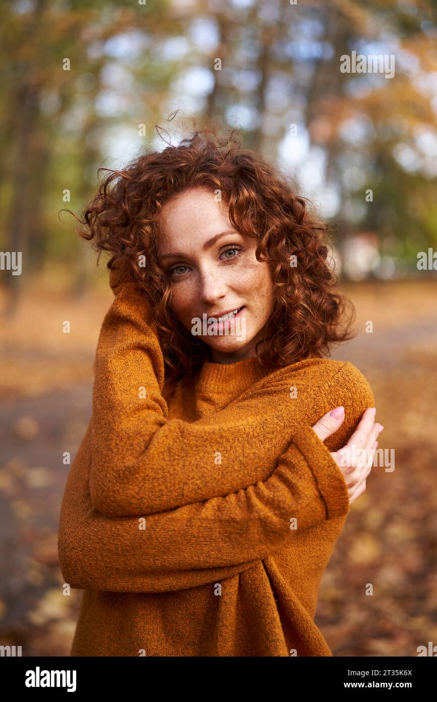 Donna sorridente a testa rossa che indossa un maglione al parco autunnale Foto Stock
