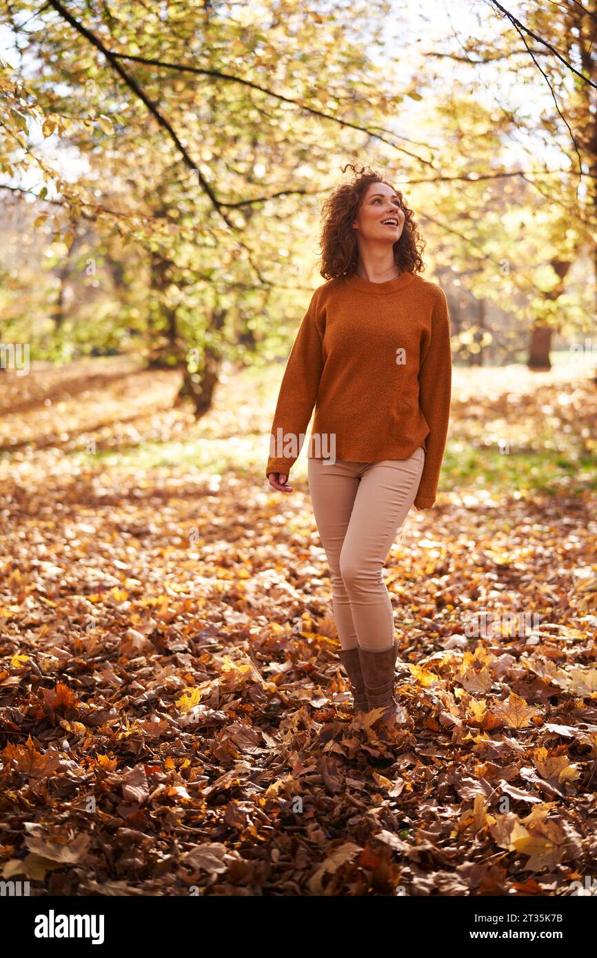 Donna rossa in piedi sulle foglie autunnali al parco Foto Stock