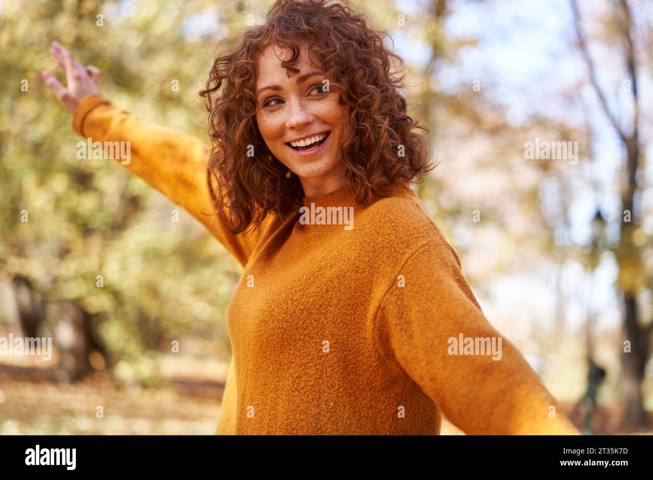 Allegra donna rossa con le braccia tese al parco autunnale Foto Stock