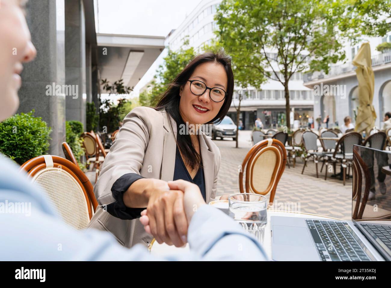 Partner commerciali che fanno stretta di mano al tavolo del caffè sul marciapiede Foto Stock