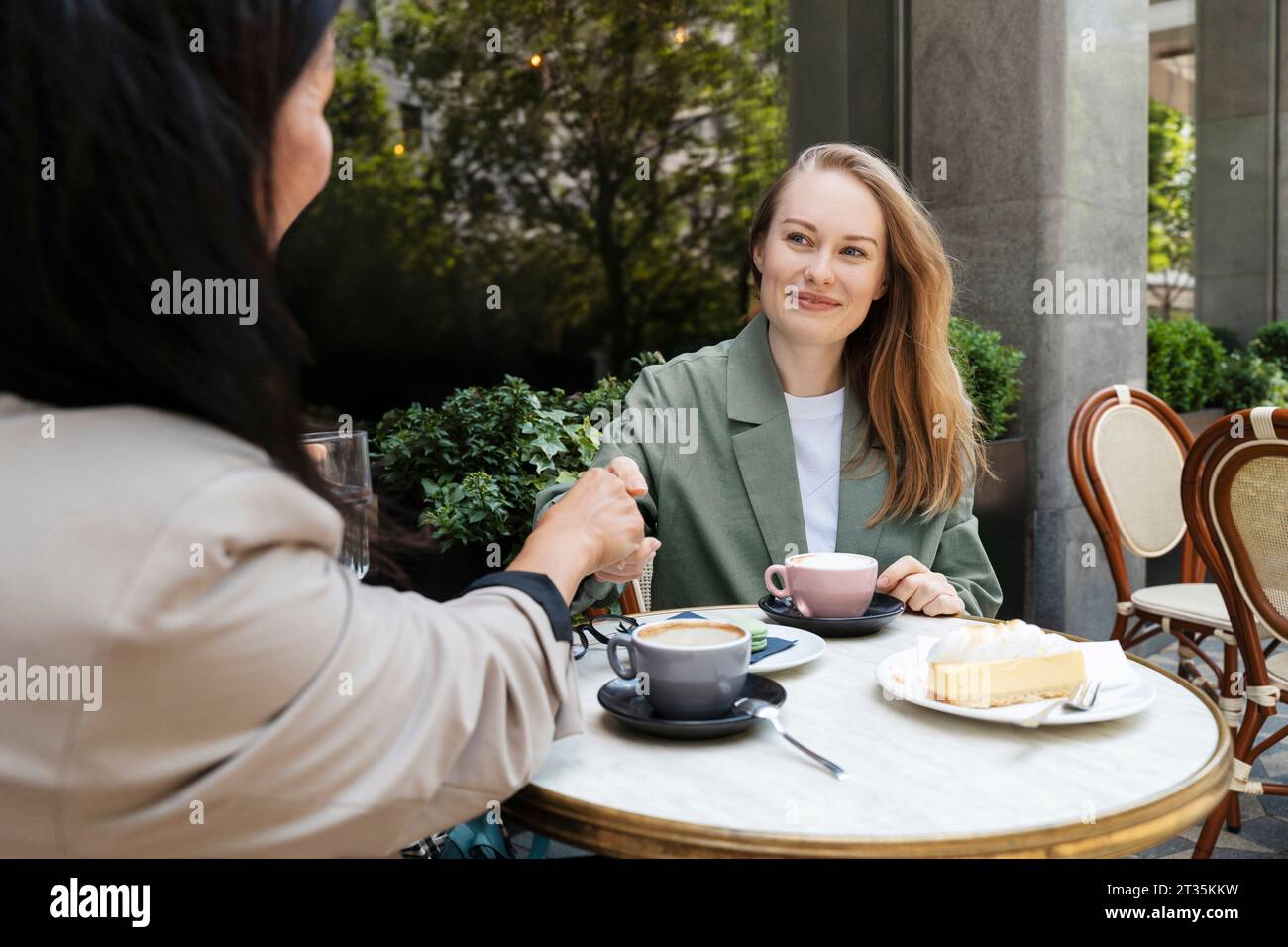 Partner commerciali che fanno una stretta di mano con tazze di caffè sul tavolo del caffè sul marciapiede Foto Stock