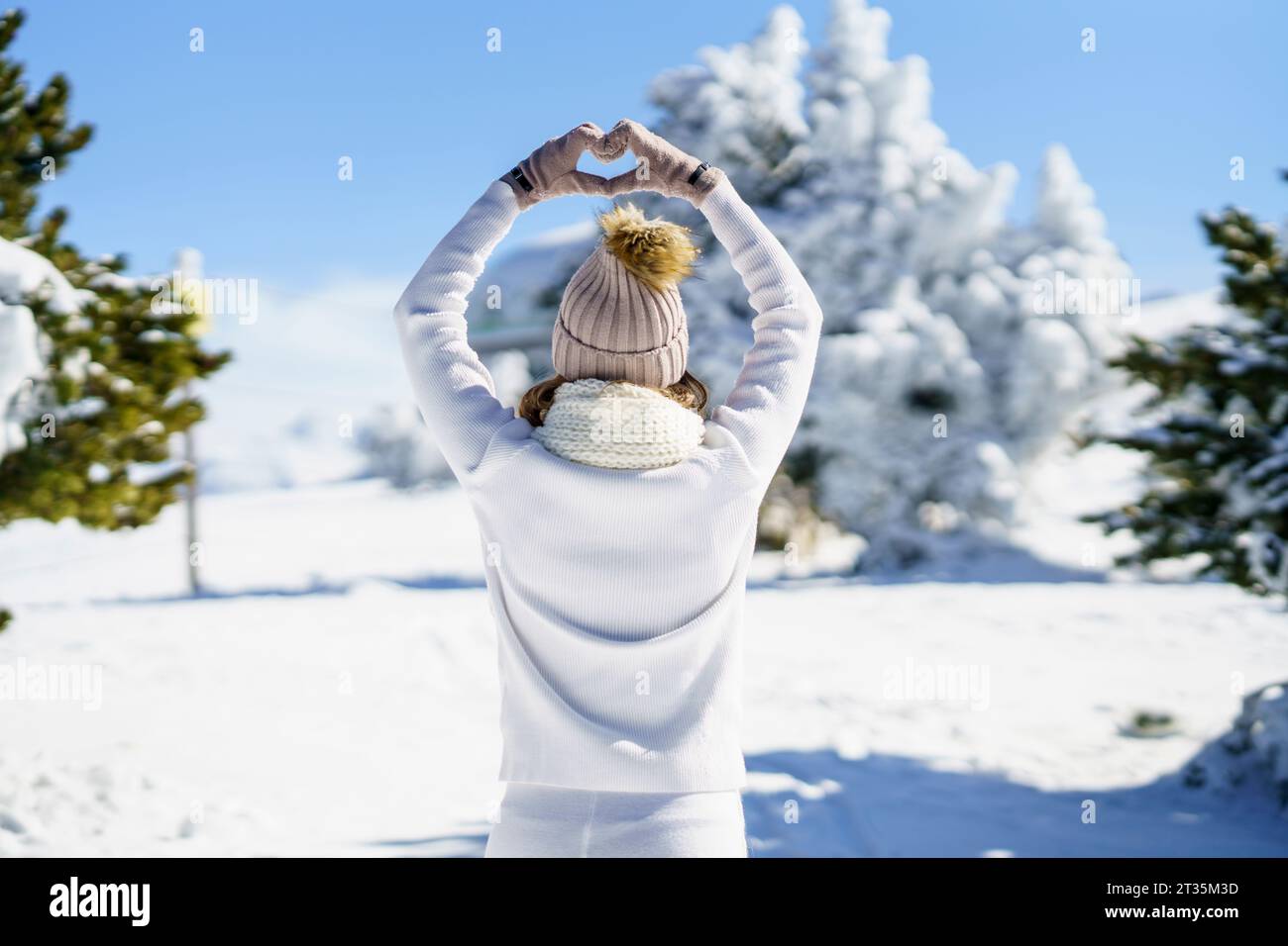 Donna con abito bianco che forma il cuore nel paesaggio invernale Foto Stock